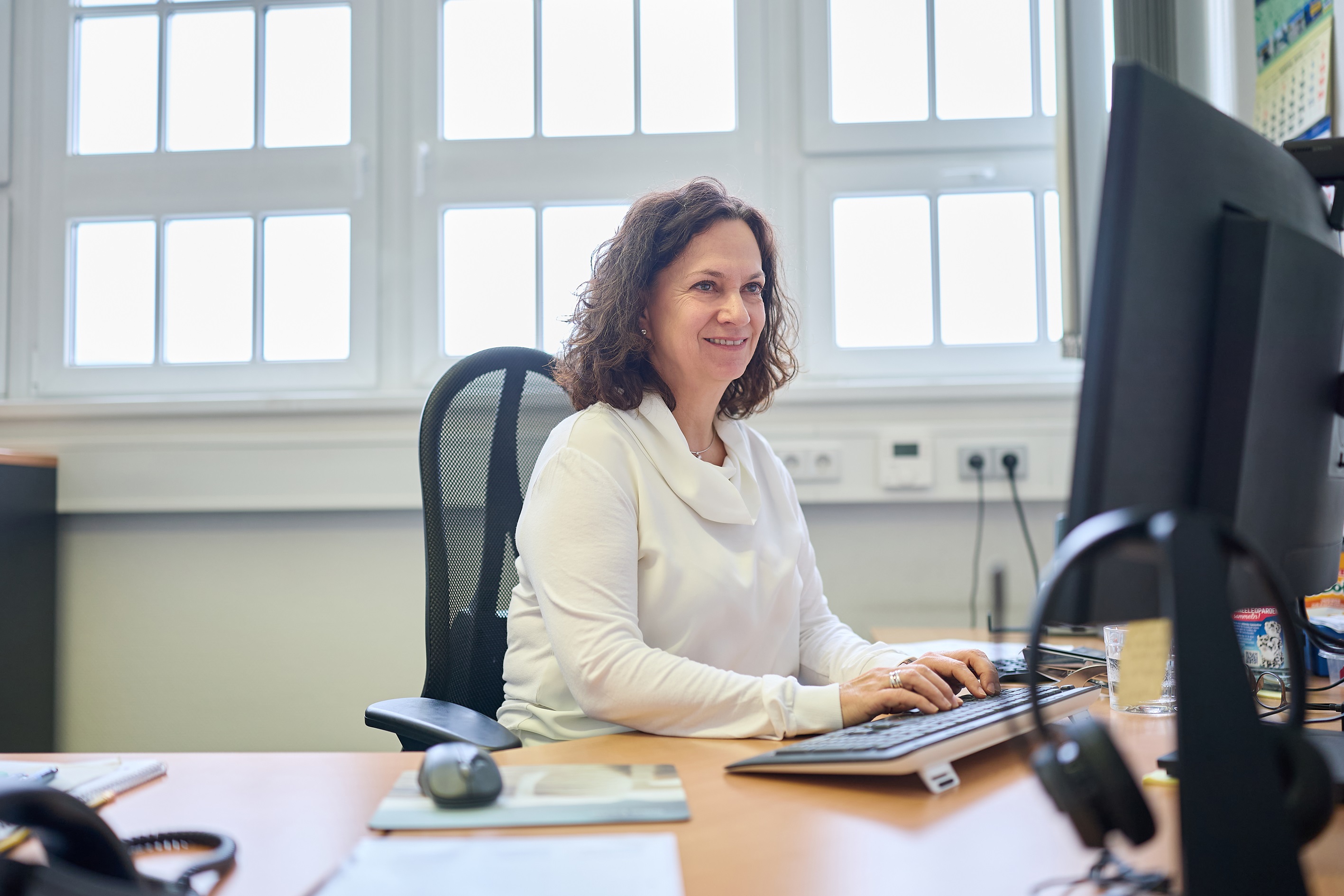 Woman in white pullover sitting at desk.